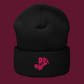 Black beanie with pink text on a purple background